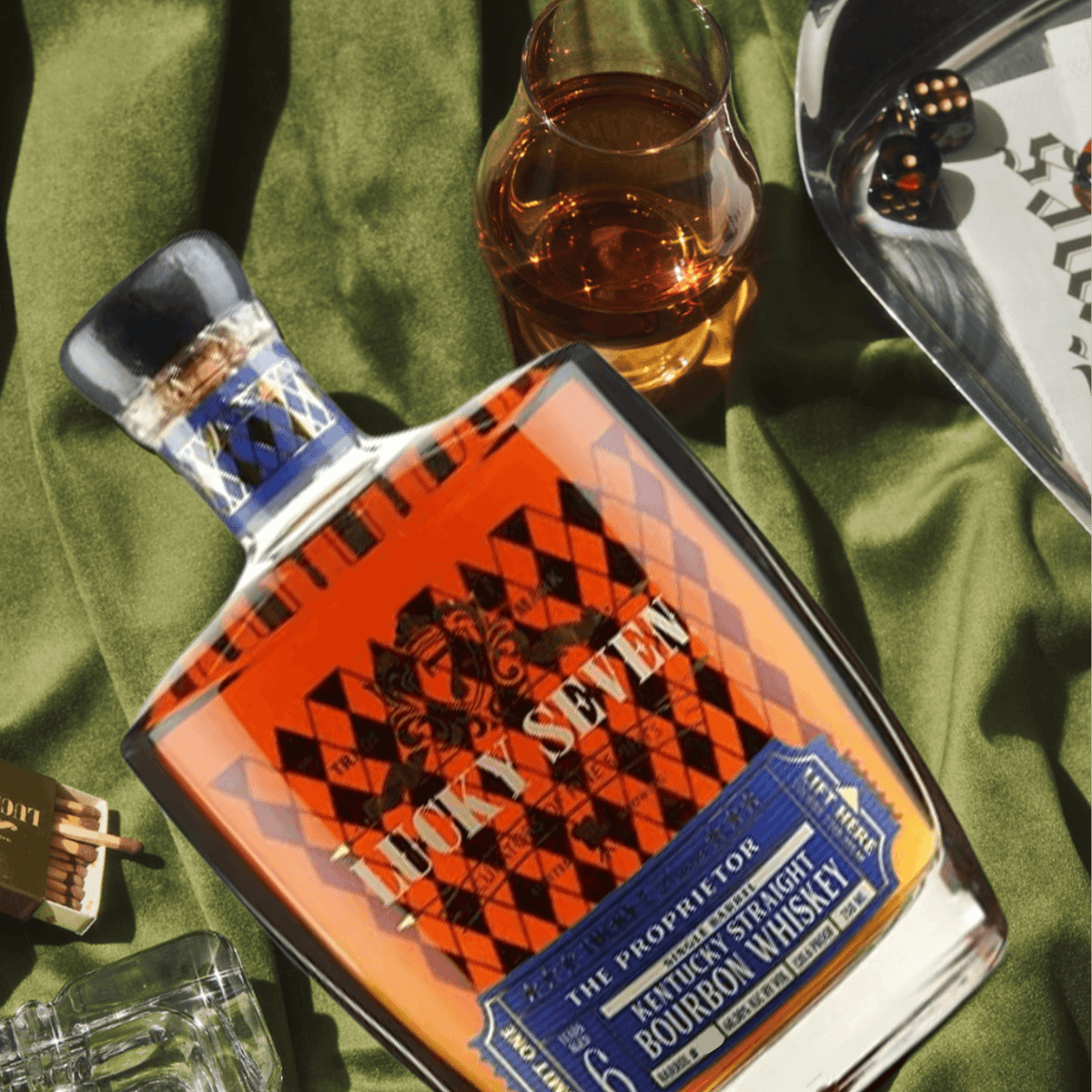 Lucky Seven The Proprietor Single Barrel 6 Year Bourbon bottle displayed with whiskey glass and dice on green velvet.