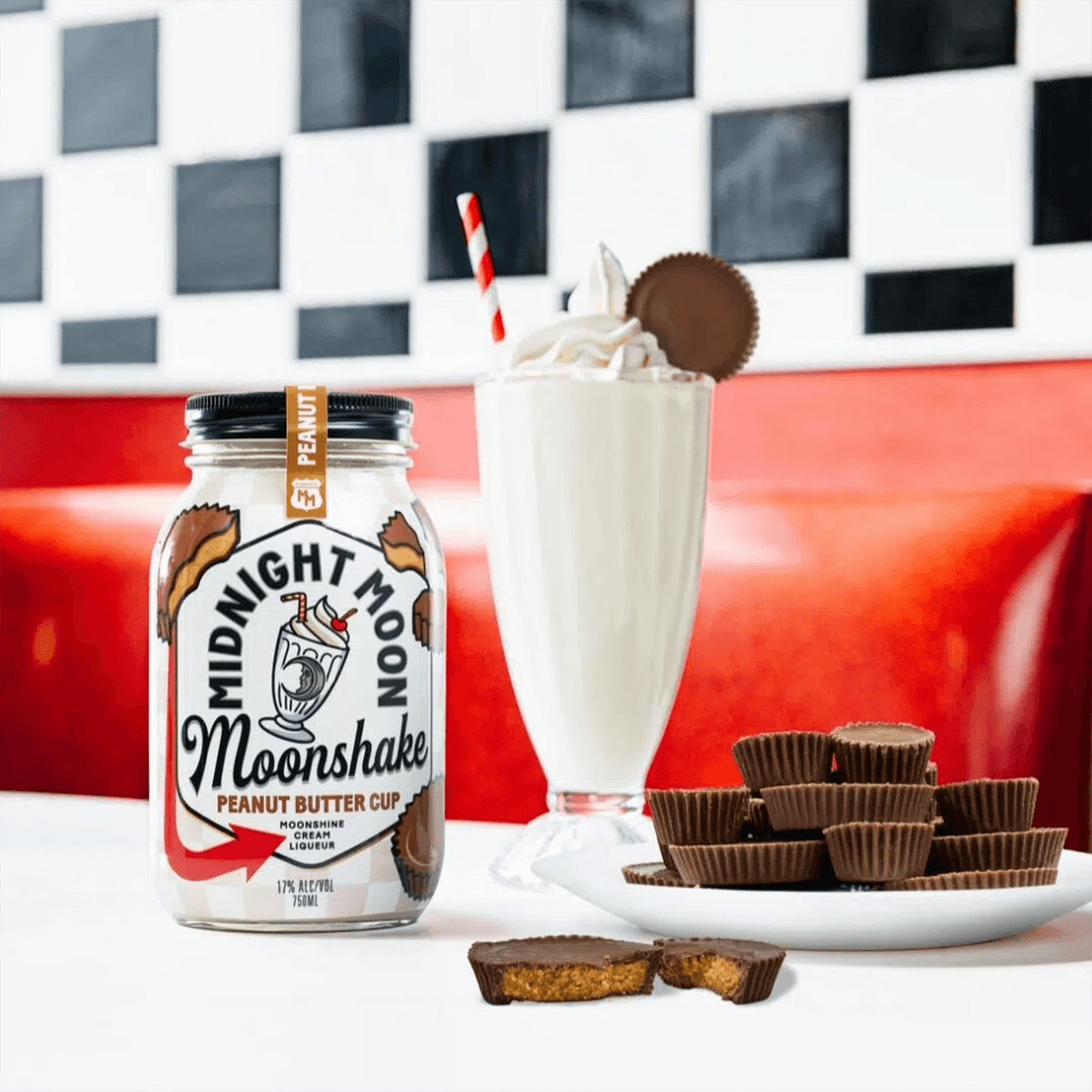 Midnight Moon Peanut Butter Cup Moonshake liqueur with a milkshake and Reese's cups on a red table.