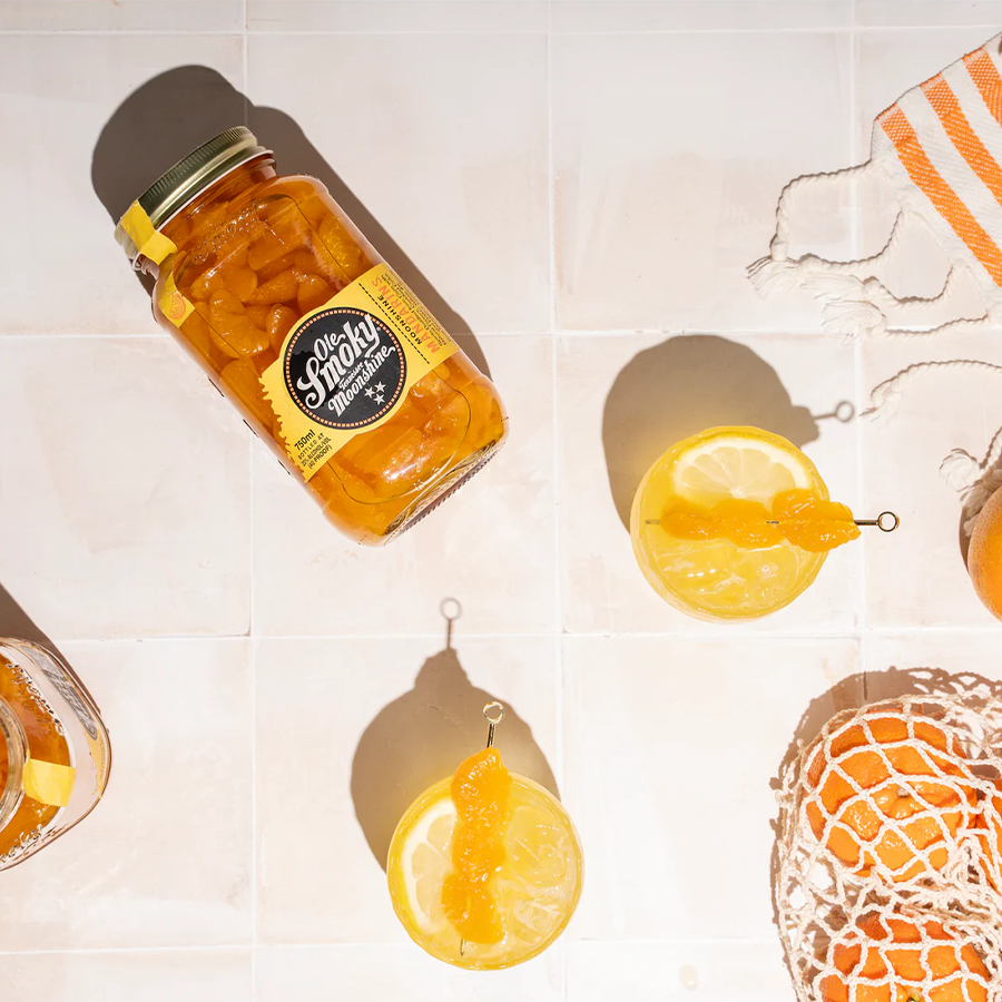 Ole Smoky Mandarins Moonshine jar with mandarin slices and cocktails on a light background