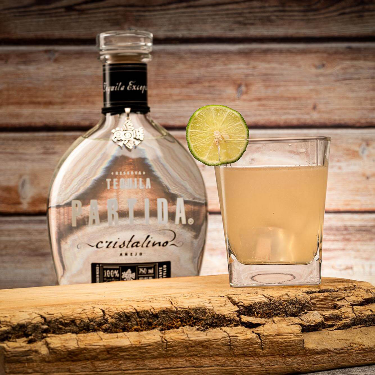 Partida Cristalino Anejo Tequila bottle with a glass and lime on rustic wood background.