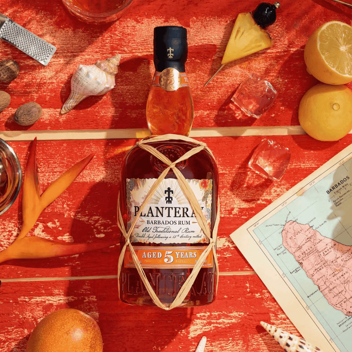 Planteray Barbados 5 Year Rum bottle surrounded by tropical fruits and seashells on a vibrant red background.