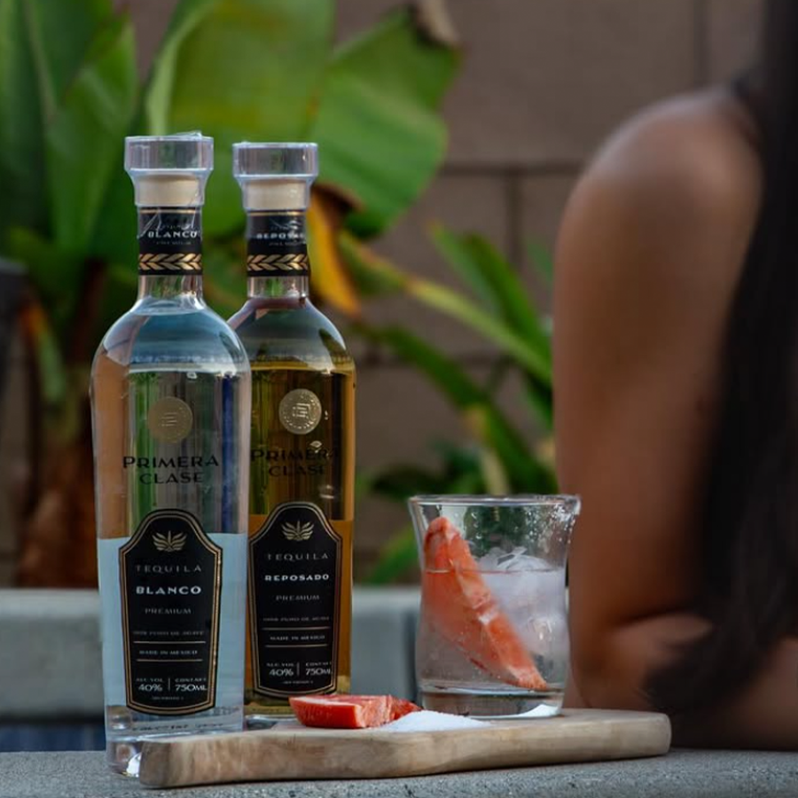 Bottles of Primera Clase Reposado and Blanco tequila with a glass and garnished fruit.