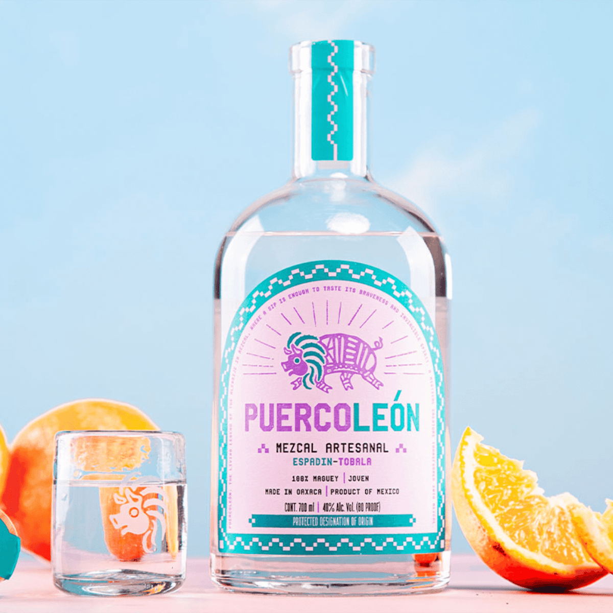 PuercoLeón Espadin-Tobala Mezcal bottle 700ml with citrus fruits and shot glass, handcrafted in Oaxaca.