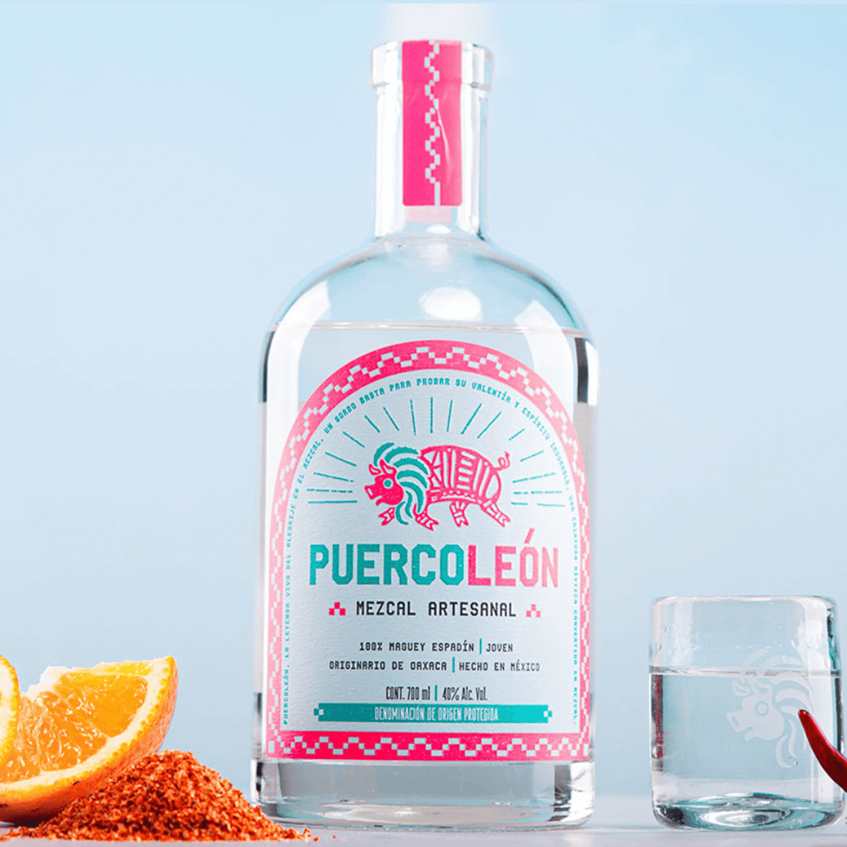 Bottle of PuercoLeón Espadin Joven Mezcal 700ml with orange and glass, highlighting its artisanal quality from Oaxaca.