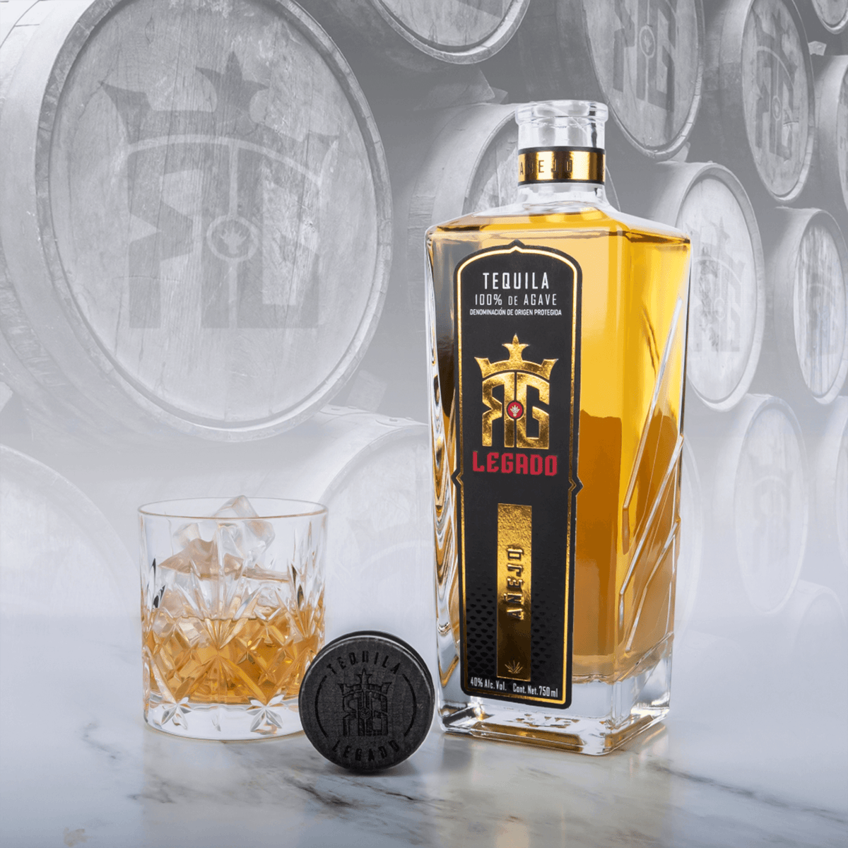 RG Legado Añejo Tequila bottle with a glass and ice, showcasing rich color and texture against barrel background.