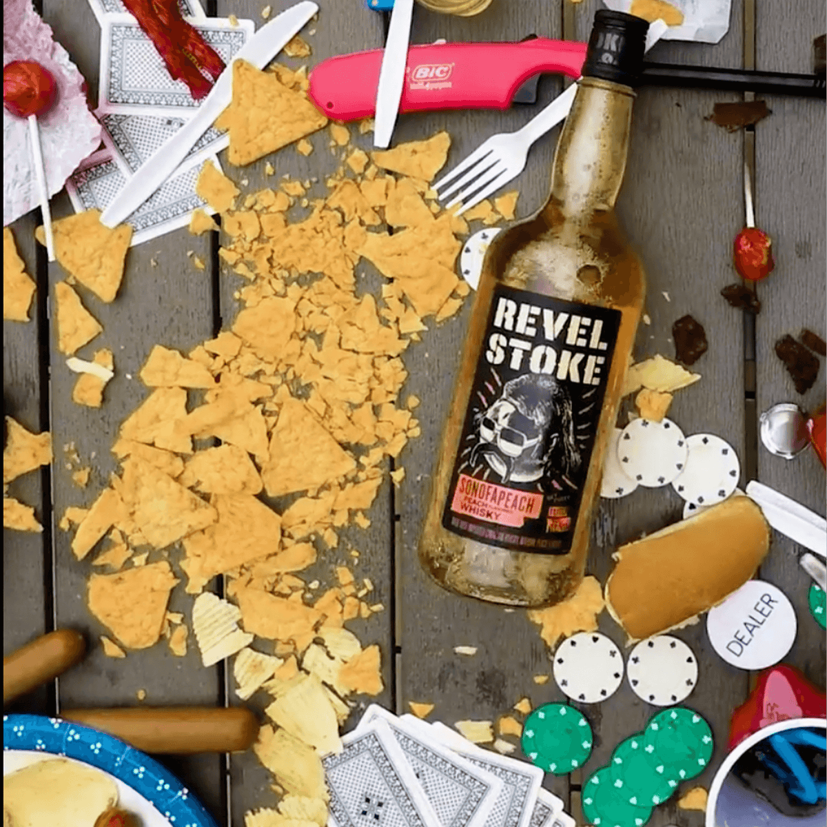 Messy tabletop scene with Revel Stoke SonofaPeach whisky bottle surrounded by snacks and poker chips.