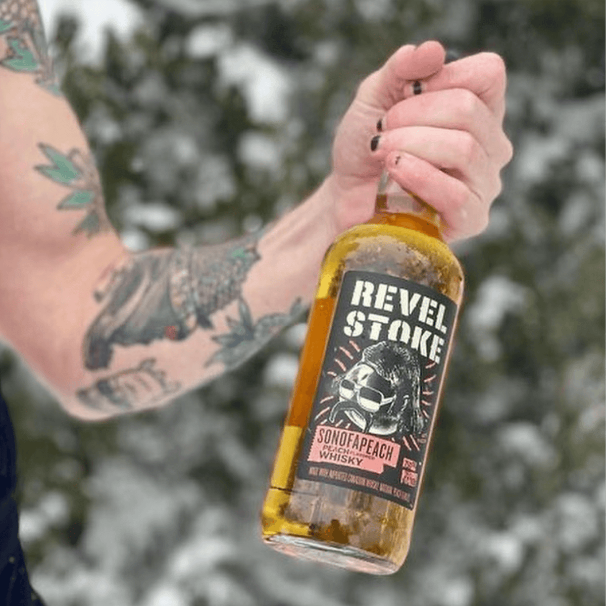 A person holding a bottle of Revel Stoke SonofaPeach Whisky outdoors in winter, showcasing bold peach flavor.