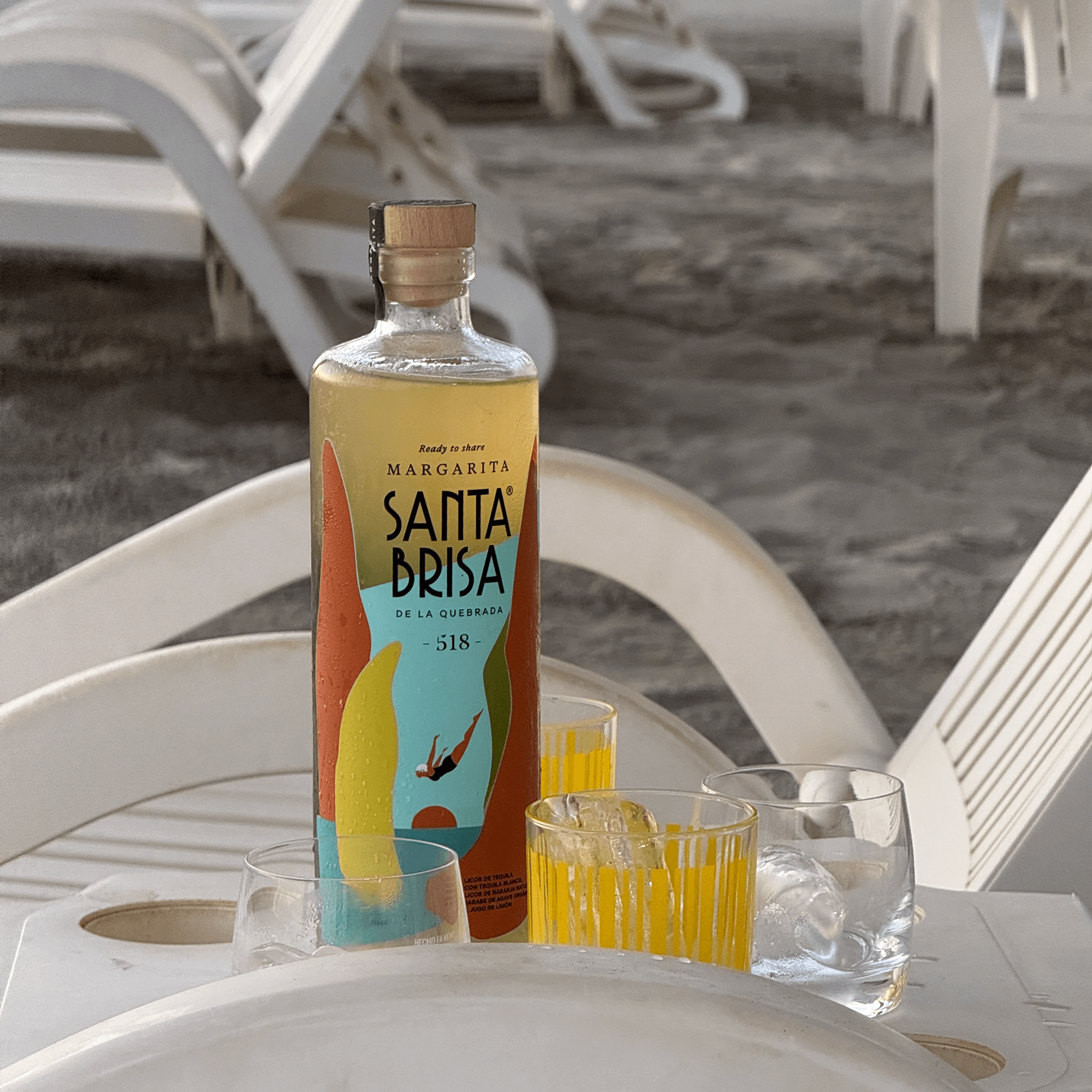 Santa Brisa Margarita cocktail bottle surrounded by glasses on a beach setting, showcasing vibrant colors and summer vibes.