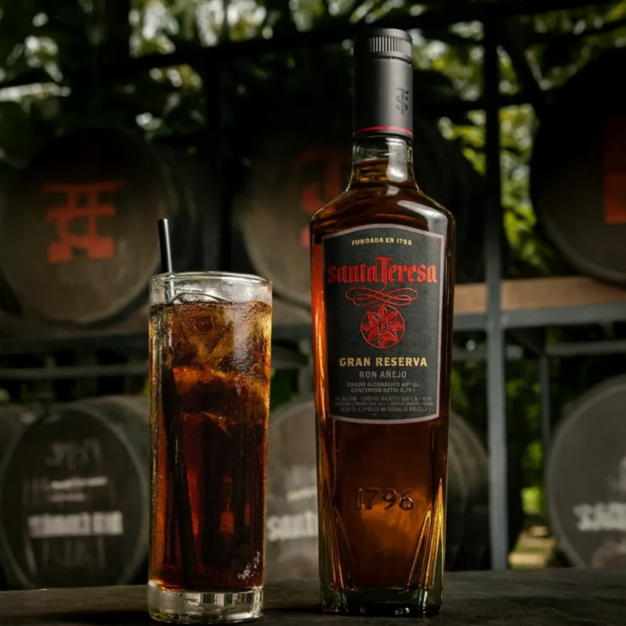Santa Teresa Gran Reserva Ron Añejo bottle and cocktail on a rustic wooden background with barrels.