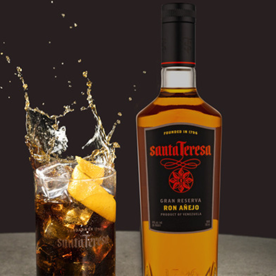 Santa Teresa Gran Reserva Ron Añejo bottle next to a glass of rum cocktail with splashes and a lemon twist.