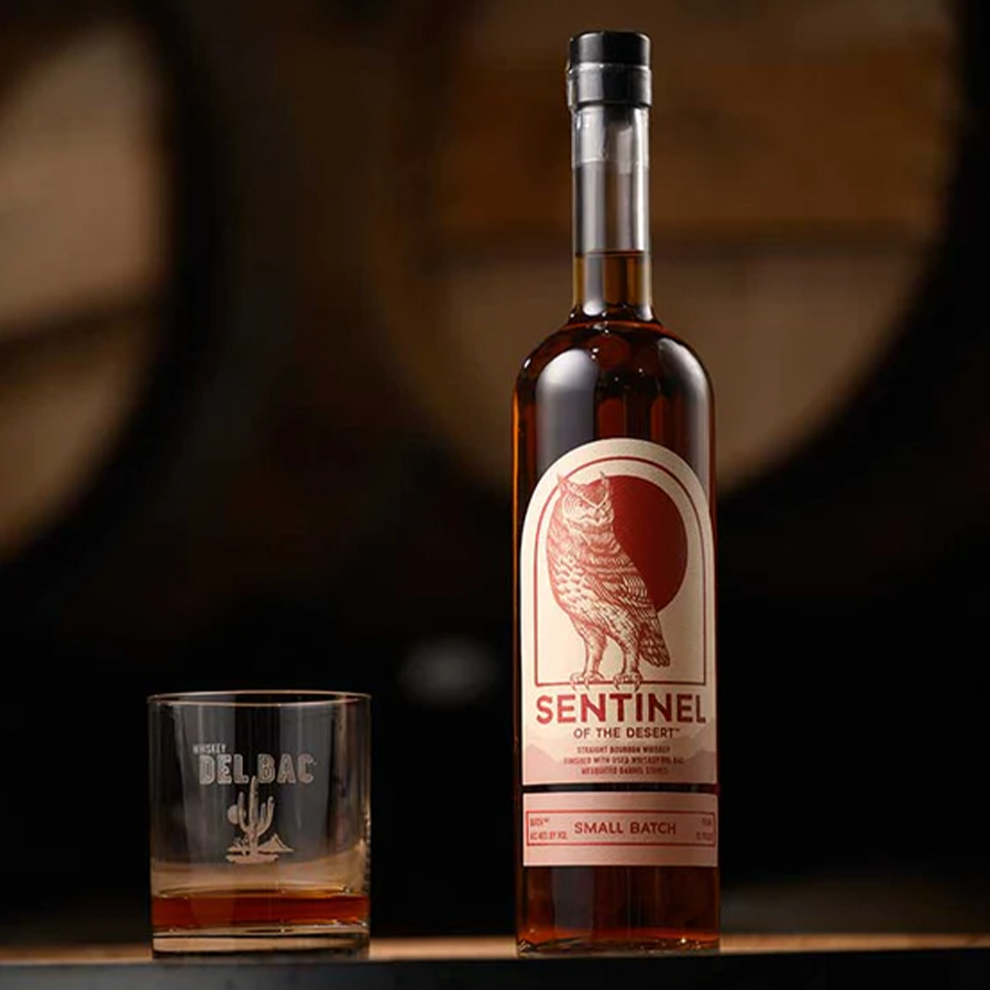 Bottle of Sentinel Bourbon of the Desert next to a glass, showcasing its unique label and small batch heritage.