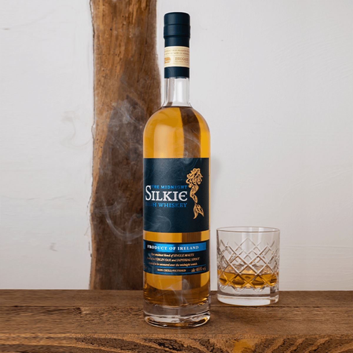 Sliabh Liag The Midnight Silkie Irish Whiskey bottle with glass on wooden table, showcasing its smoky blend.