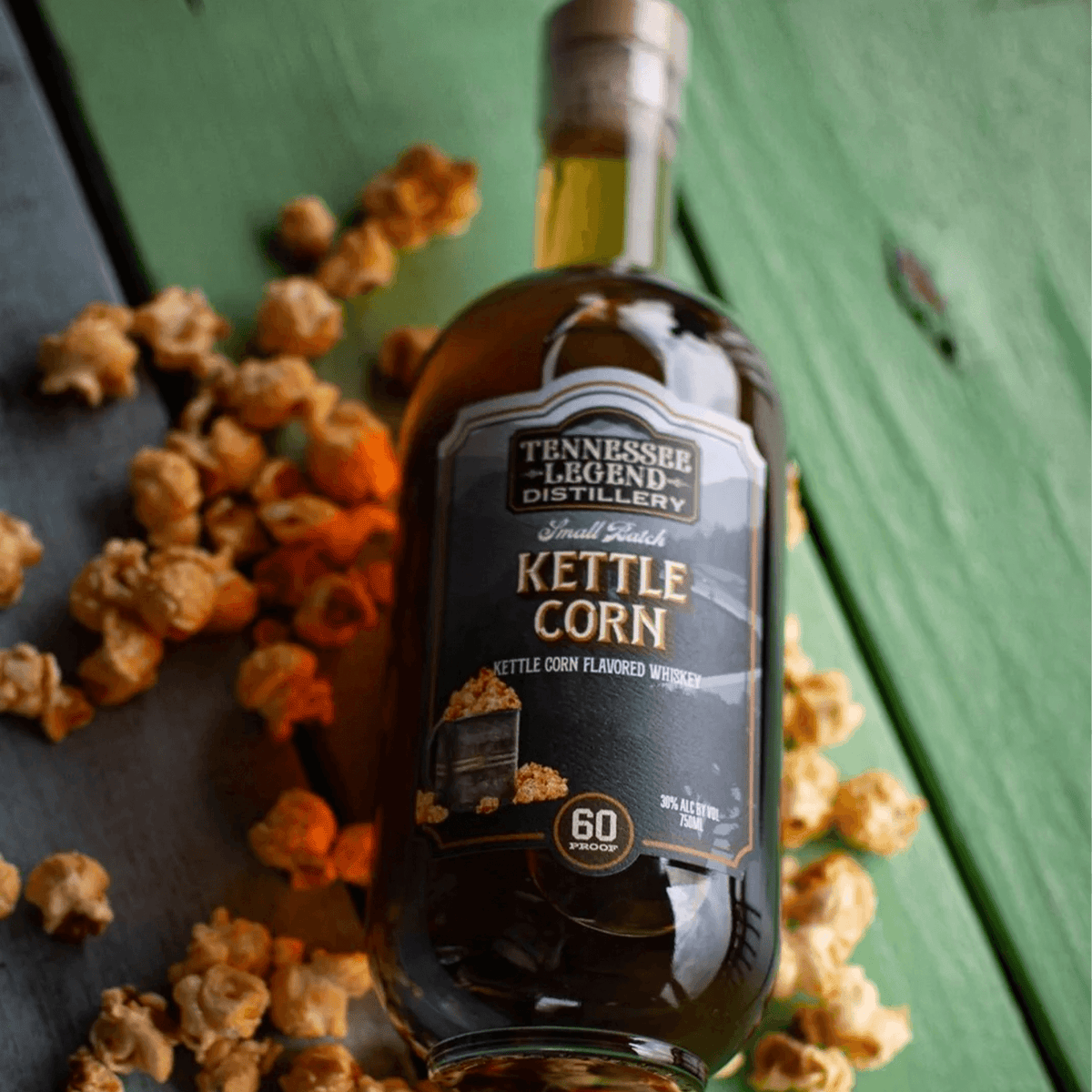 Tennessee Legend Kettle Corn Whiskey bottle surrounded by popcorn on a green wooden surface.