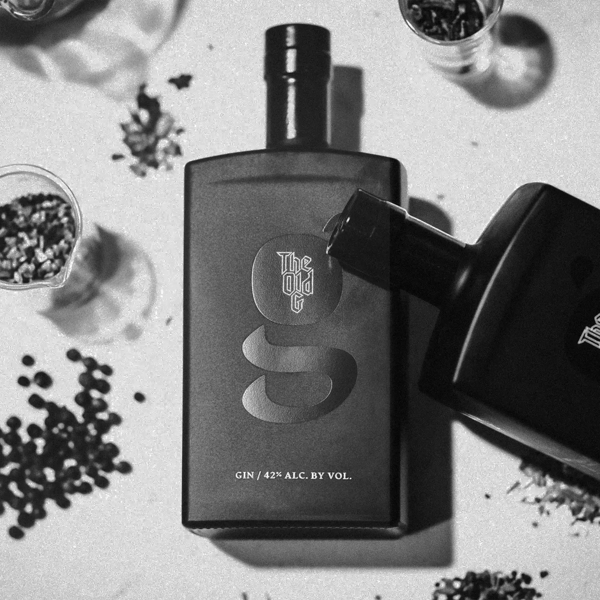 The Old G Gin bottle surrounded by botanicals on a textured surface, showcasing premium quality and smoothness.