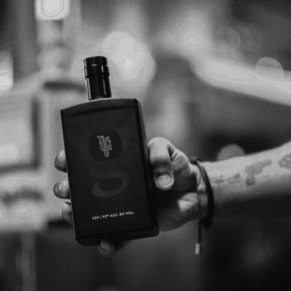 Hand holding a bottle of The Old G Gin, crafted for smoothness and infused with botanicals, perfect for cocktails.