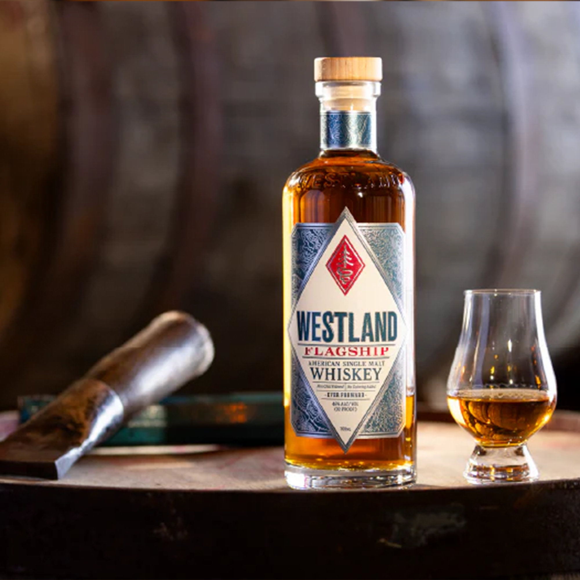 Westland Flagship American Single Malt Whiskey bottle with glass on a wooden barrel background.