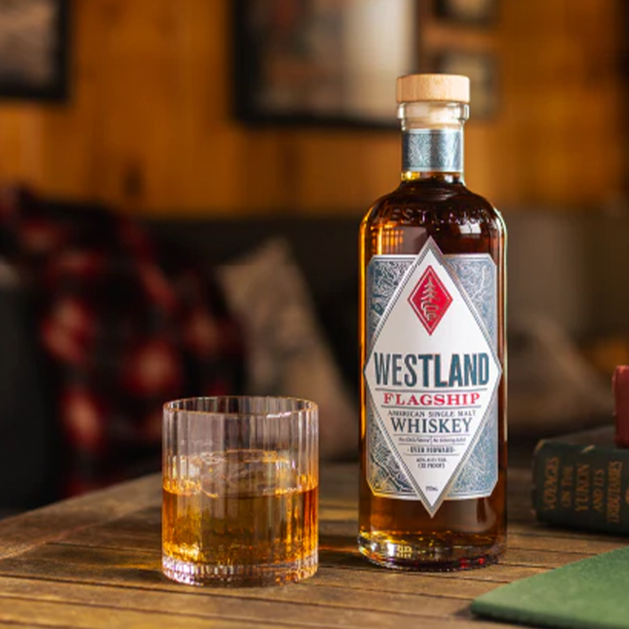Bottle of Westland Flagship American Single Malt Whiskey with a glass of whiskey on a wooden table.
