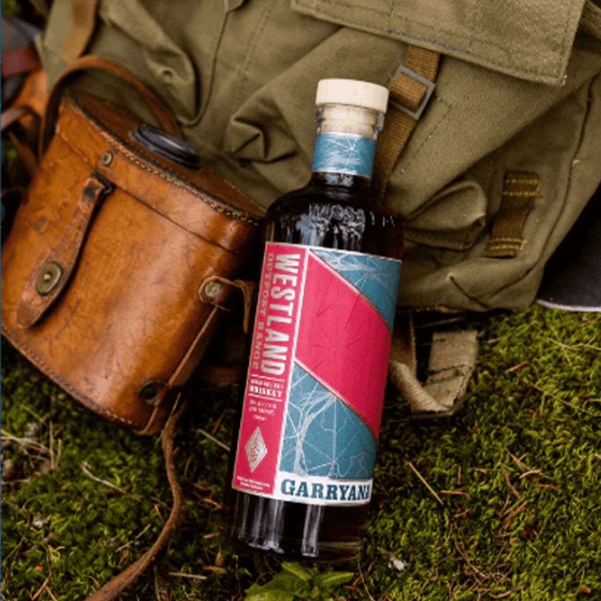 Westland Garryana 9th Edition 700ml bottle on grass near a vintage backpack and leather bag.