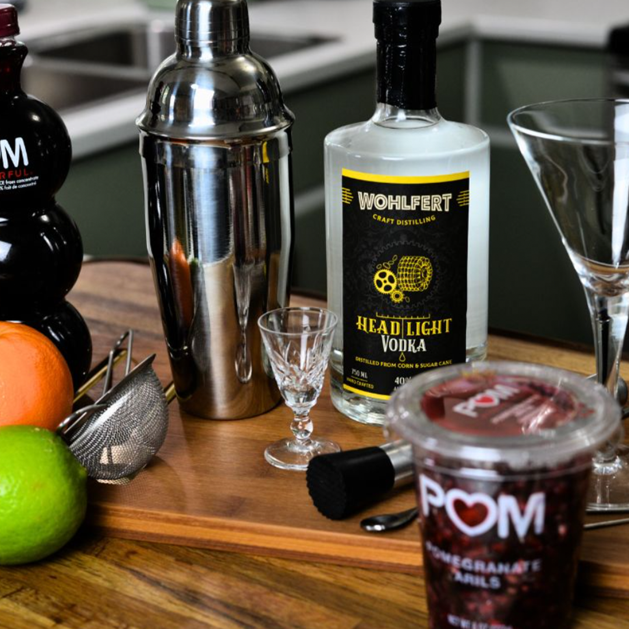 Wohlfert Headlight Vodka bottle on a wooden bar with cocktail shaker, glasses, and fresh fruits for mixing drinks.