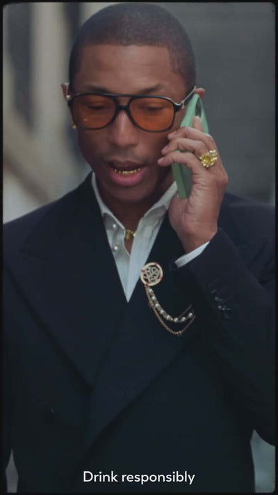 Pharrell Williams in a stylish outfit, talking on the phone, promoting responsible drinking.