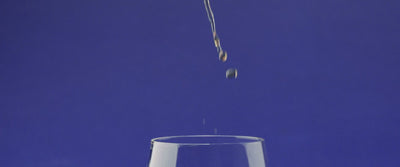 Droplets falling into a glass against a vibrant blue background, evoking the enjoyment of whiskey tasting.